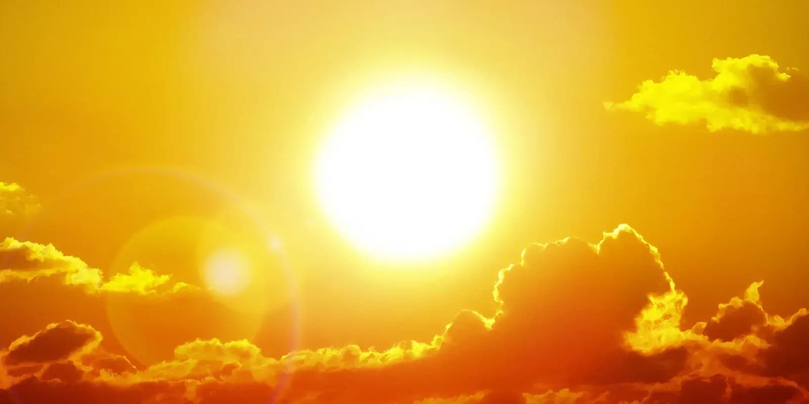A blazing white sun burns in a deep yellow and orange sky above a low band of backlit clouds.