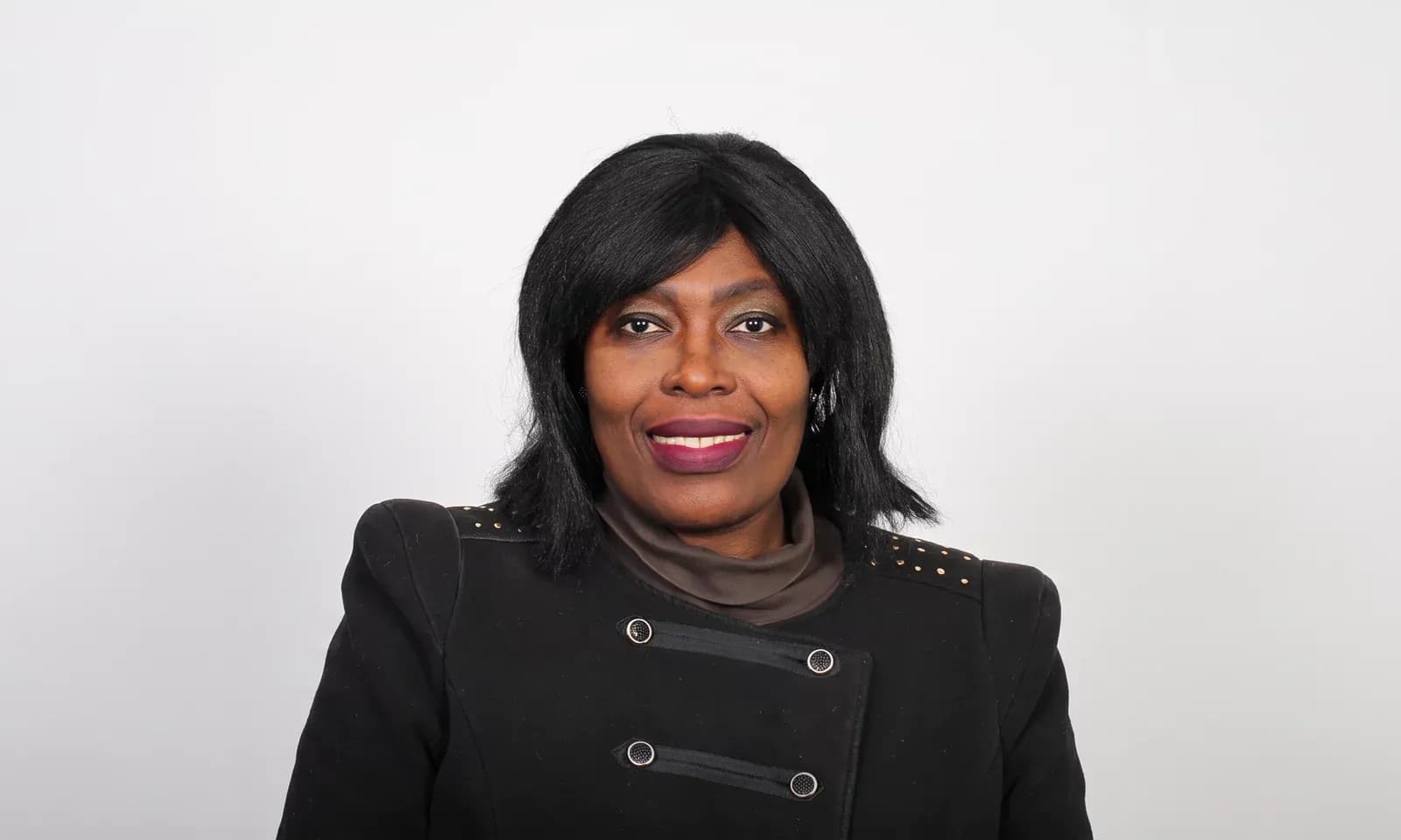 Dr I. Fortune Glavee in a black jacket against a light grey studio backdrop