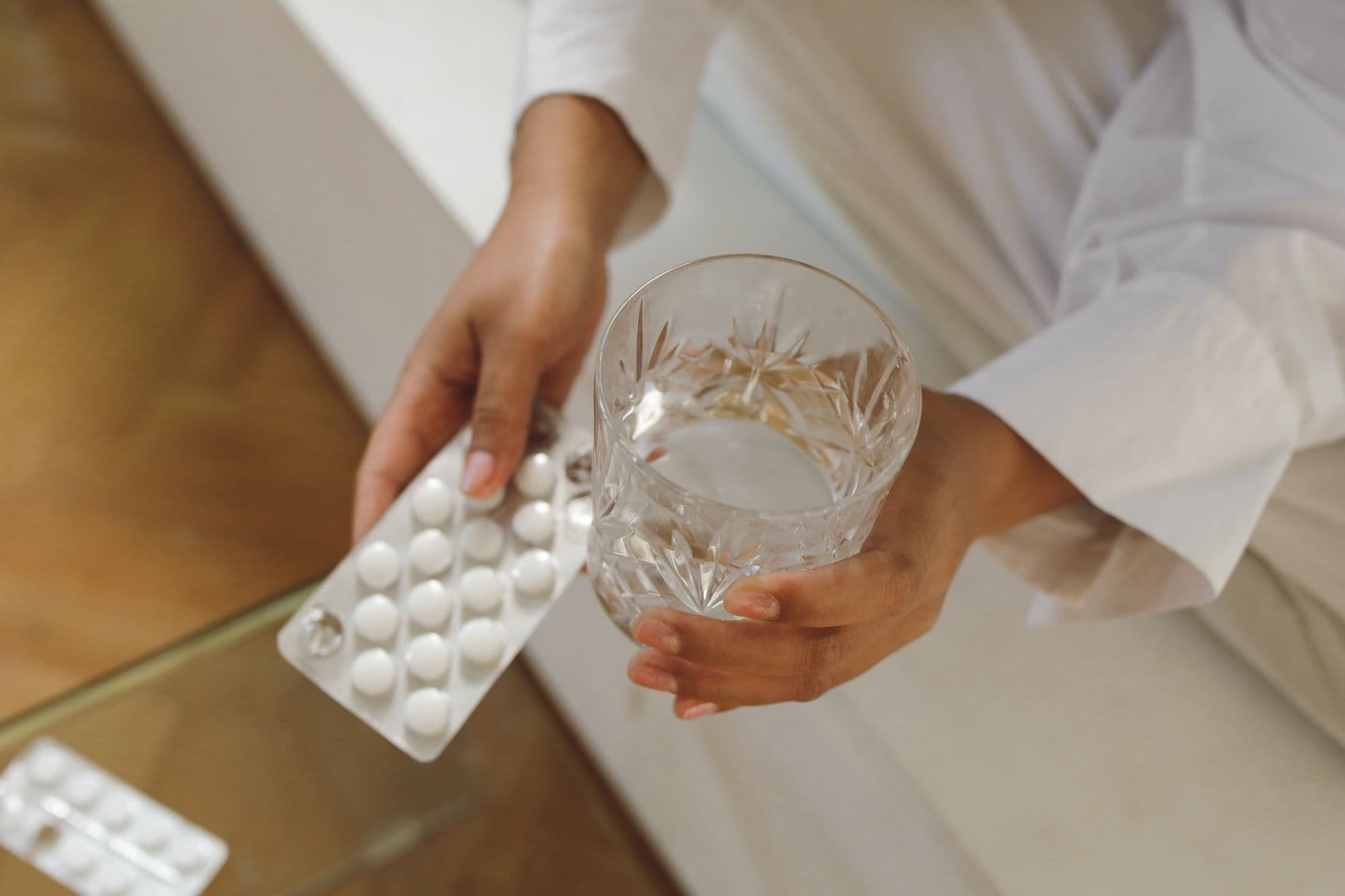 Close-up of hands holding a blister pack of pills and a glass of water