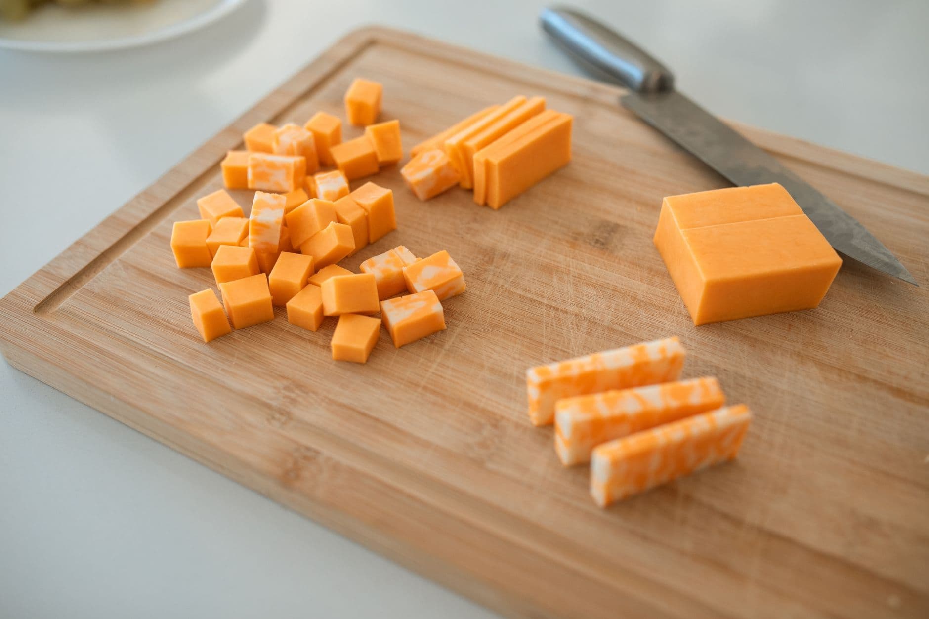 Cubes and slices of cheddar and marbled jack cheese on a wooden cutting board with a knife